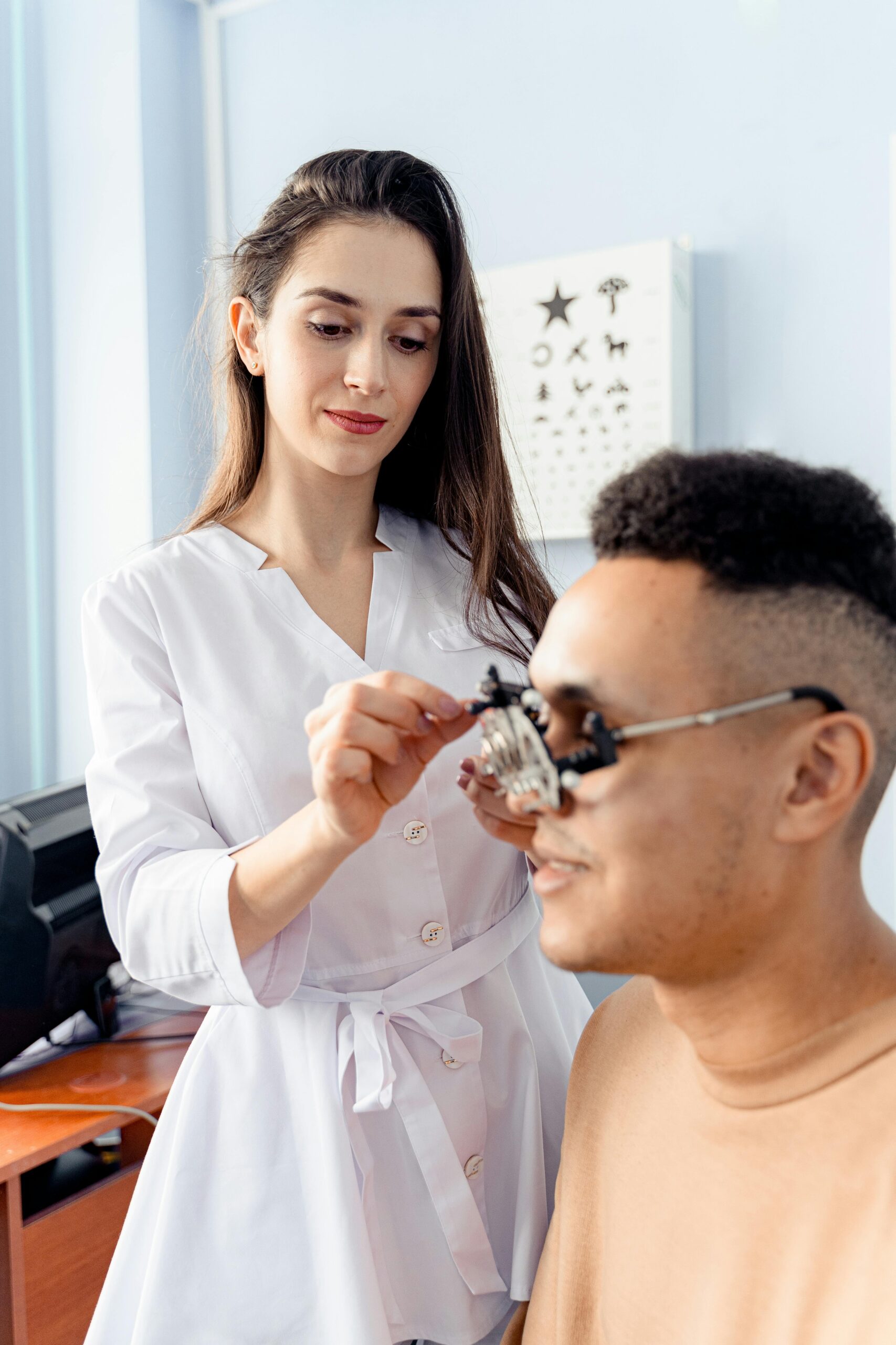A female optometrist adjusts an optical trial lens frame during an eye examination of a male patient.